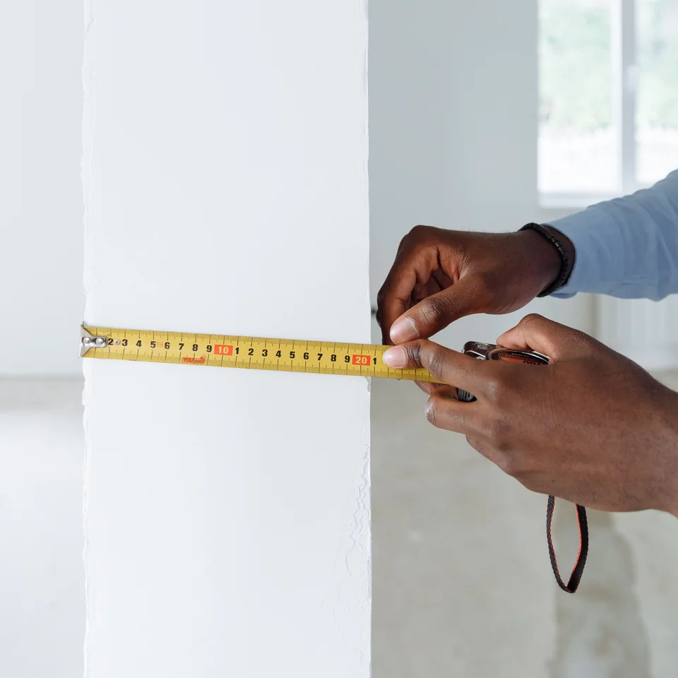 Hands using a tape measure at a white interior wall; general measurement scene
